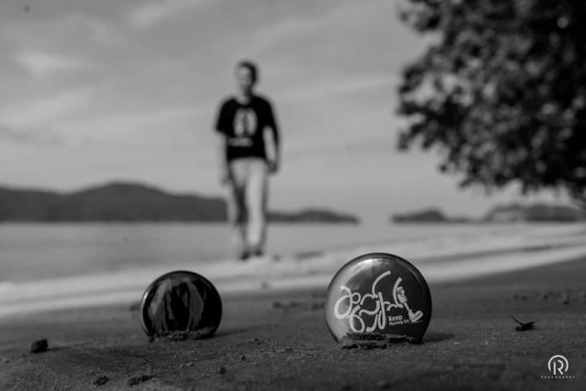 Black and white photo of Keep Moving On badges in the sand with a person walking in the distance.