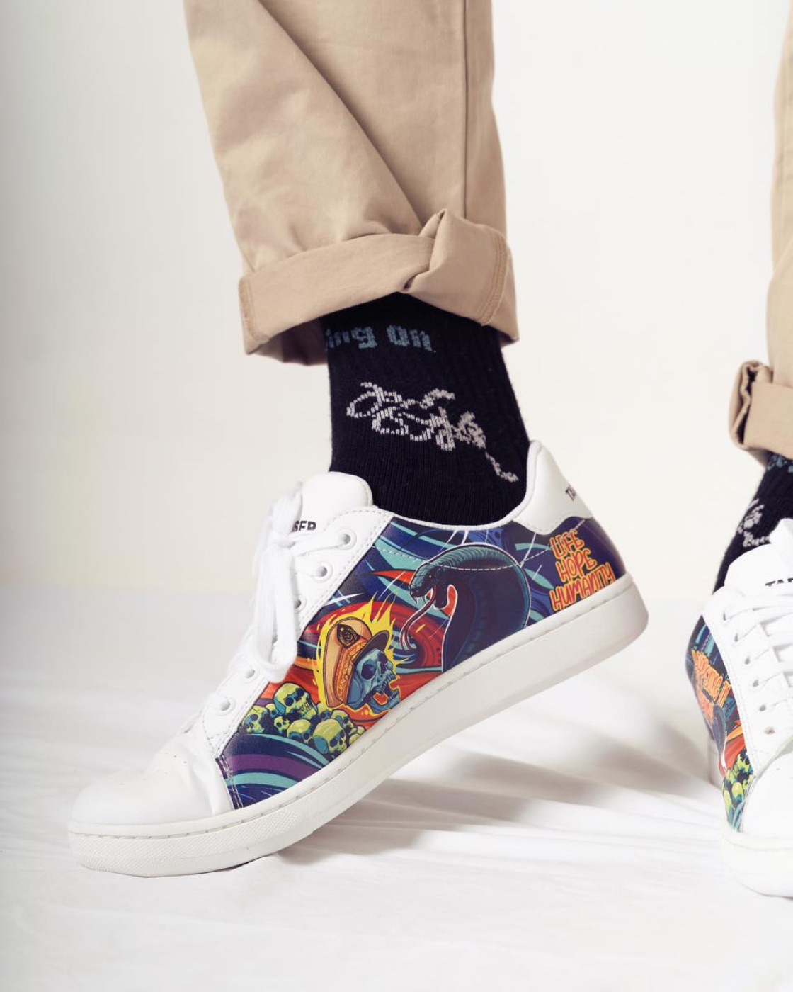 Close-up of artwork sneakers reading Life Hope Humanity, worn with black Keep Moving On socks.