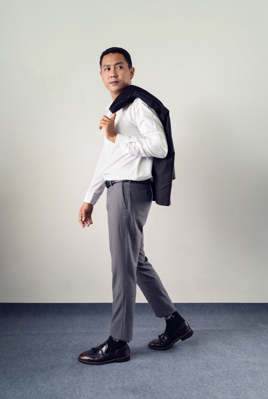 Man in a white shirt walking with a jacket over his shoulder, black socks and loafers.