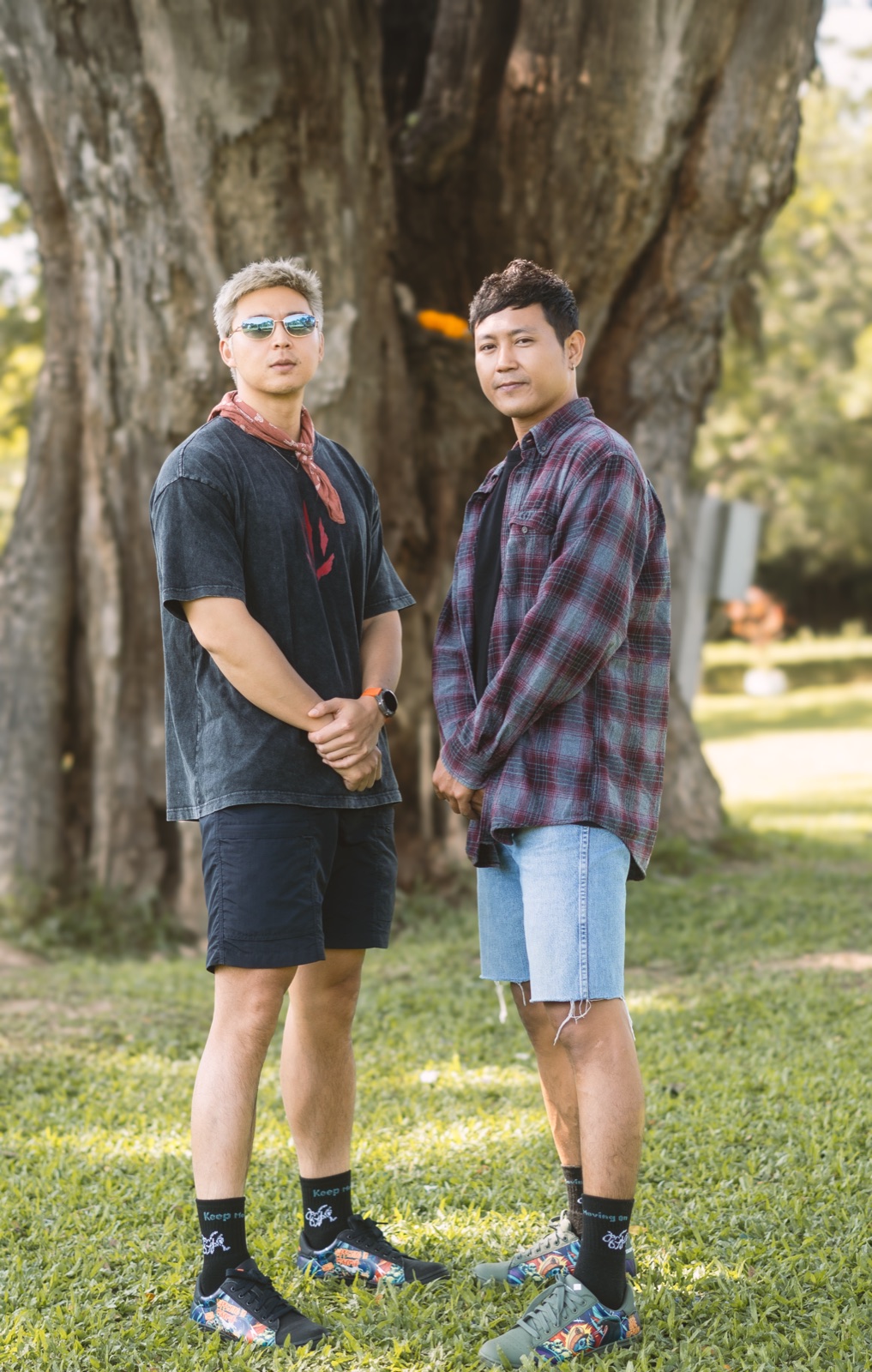Two friends standing under a huge tree wearing Keep Moving On socks and artwork sneakers.