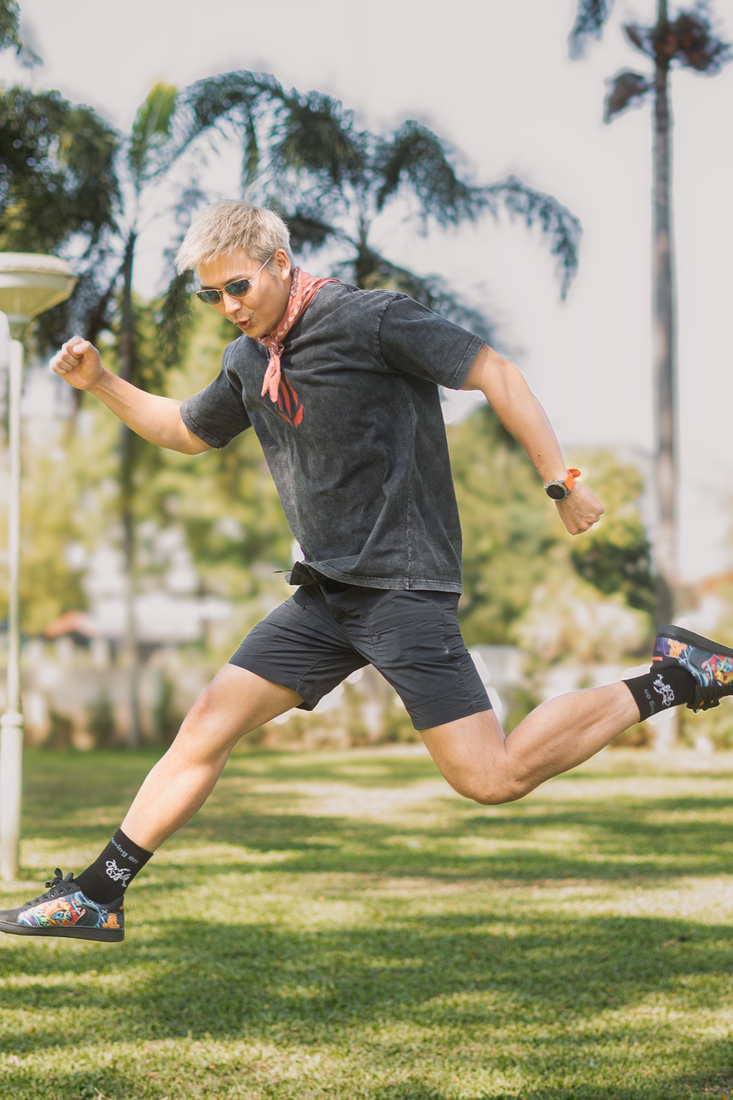 Man joyfully leaping across a lawn in black Keep Moving On socks and artwork sneakers.