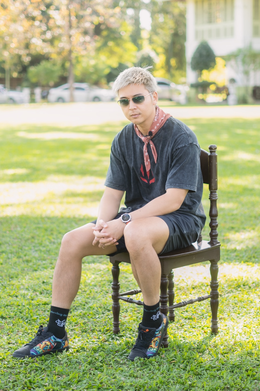 Man seated on a wooden chair on a lawn in black Keep Moving On socks and artwork sneakers.