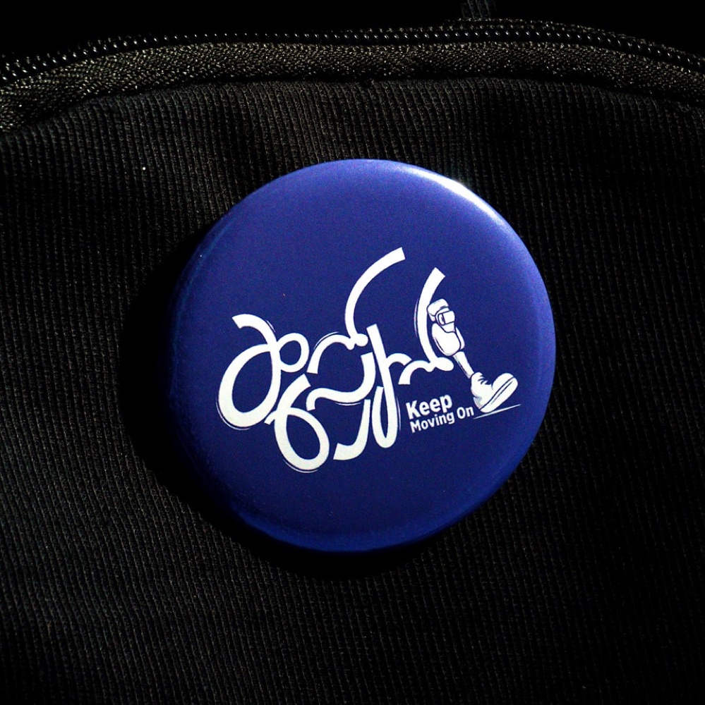 Blue Keep Moving On badge pinned to a black bag.