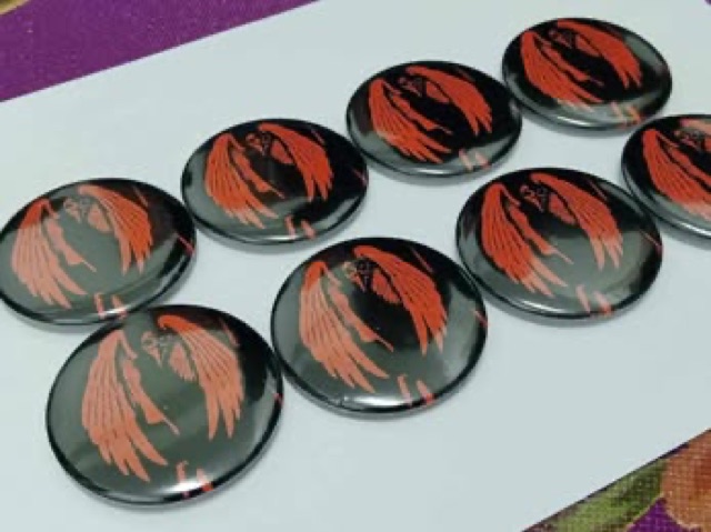 Eight badge pins with a red winged-bird design lined up on a table.