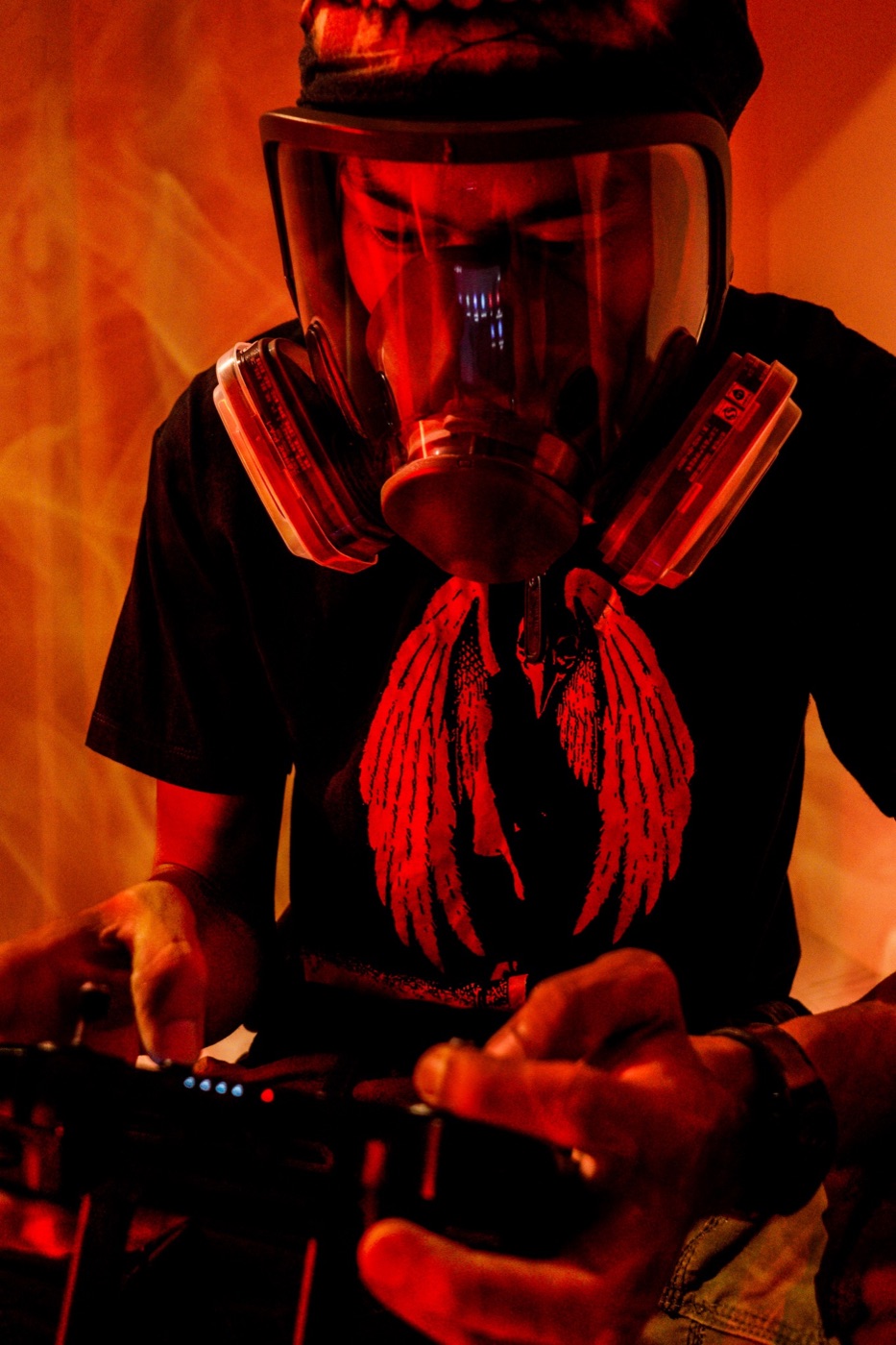 Portrait in red smoke: a person wearing a full-face respirator and a winged-bird tee.