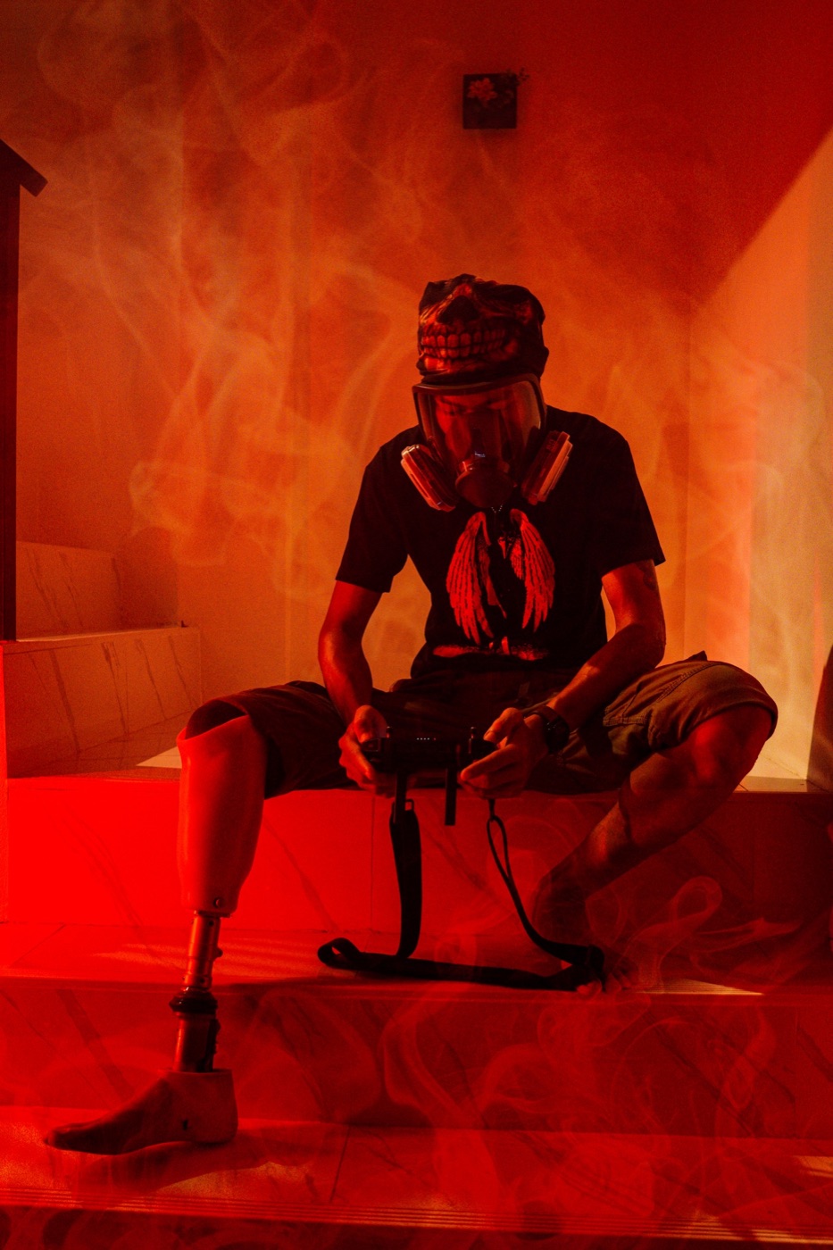 A man with a prosthetic leg sitting on steps in red-lit smoke, calmly holding a camera rig.