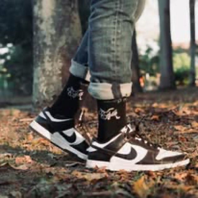 Black Keep Moving On socks worn with brown and white sneakers among fallen leaves.
